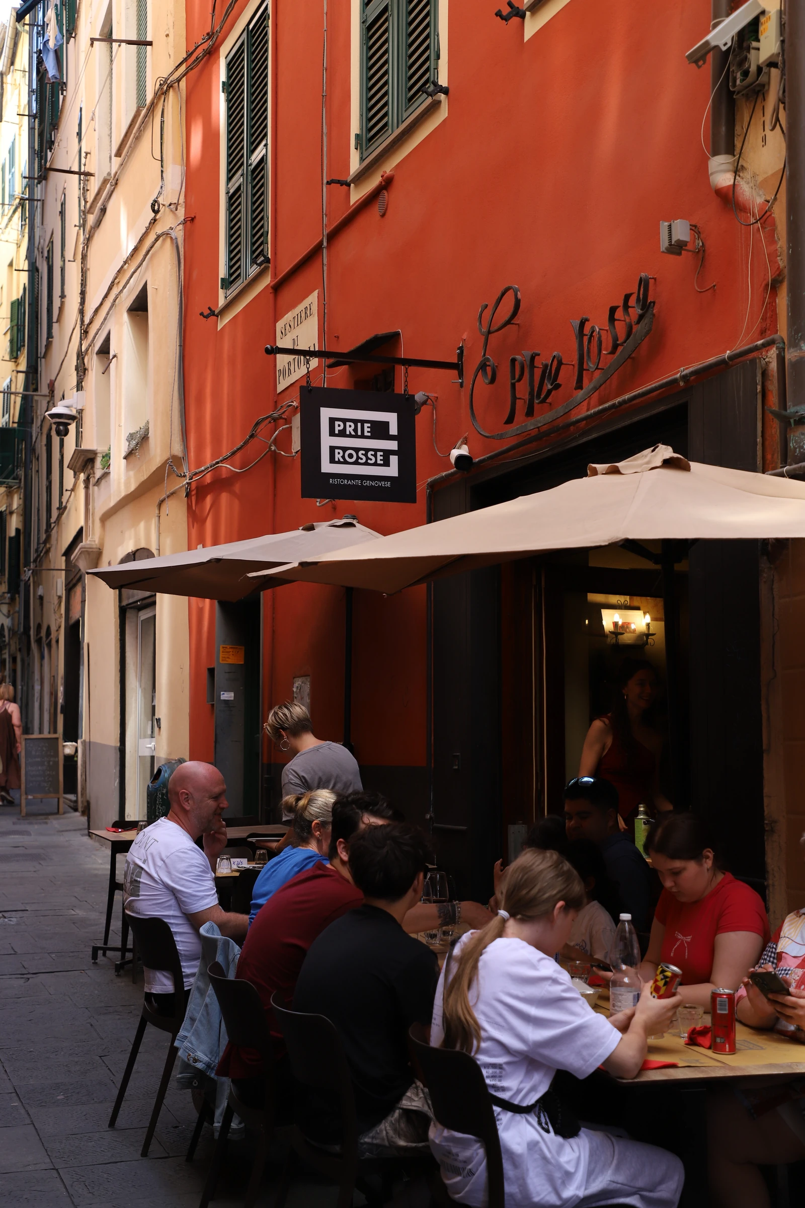 La facciata rossa di E Prie Rosse con i tavoli all'aperto nel carruggio di via di Ravecca, centro storico di Genova